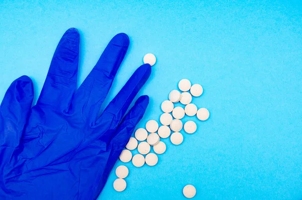 A medical blue glove and white round pills lie on a blue background in macro view from above and at an angle. Crumpled glove