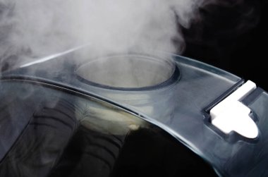 Siyah arka planda nemlendirici. Genel plan ve makro nemlendirici. Cihaz yüz ve yanlara doğru. Makroda buharlı su. Siyah navigasyon çubuğu, nemlendirici beyaz dokunmatik tuşları kontrol ediyor. Benimki, buhar bölmesi, giriş, işlem.