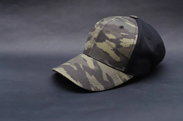 Men\'s two-tone cap on a black background. The baseball cap is black at the back, front and visor of the military workshop, khaki camouflage. Men\'s black cap with camouflage in macro. Side view, stern, top. Cap closure, button on top, ventilation hole