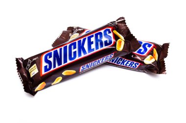 Haziran 2020. Kiev, Ukrayna. 50 gramlık iki küçük çubuk, beyaz arka planda bir haç şeklinde birbiri üzerine yatar. Makro olarak üst ve yan görünüm. Snickers çikolatası başka bir barda yatıyor..