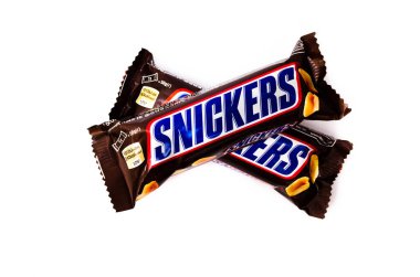 Haziran 2020. Kiev, Ukrayna. 50 gramlık iki küçük çubuk, beyaz arka planda bir haç şeklinde birbiri üzerine yatar. Makro olarak üst ve yan görünüm. Snickers çikolatası başka bir barda yatıyor..
