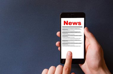 Haberler. Haberleri okuyorum. Akıllı telefon ekranındaki kırmızı yazılar siyah bir arkaplanda. Erkek eli akıllı telefonu tutuyor, tıklıyor, haberlere çıkıyor.