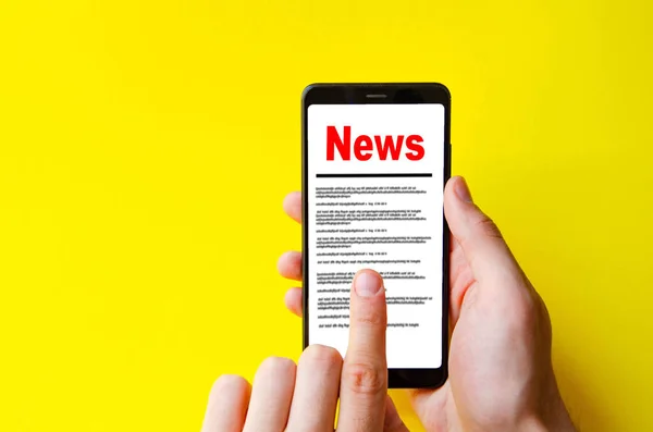 News. Reading the news. The inscription red news on the smartphone screen lies on a yellow background. Male hand holds a smartphone, clicks, leafs through the news
