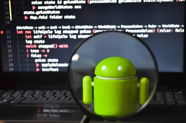 Beyaz arka planda yeşil bir android figürü ve sarı bir akıllı telefonun yanında büyüteçten bir görüntü. Android ve büyüteç. Temmuz 2020. Kiev, Ukrayna