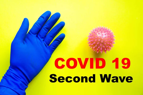 Covid 19 second wave. Covid 19. Blue medical glove and virus on blue, yellow, black background and inscription Covid 19 second wave