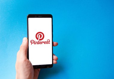 Pinterest. Mavi, sarı, siyah arka planda Pinterest akıllı telefon ekranında erkek eli ile akıllı telefon. Temmuz 2020. Kiev, Ukrayna.
