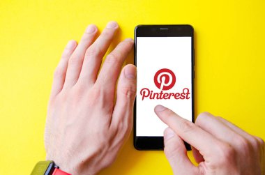 Pinterest. Mavi, sarı, siyah arka planda Pinterest akıllı telefon ekranında erkek eli ile akıllı telefon. Temmuz 2020. Kiev, Ukrayna.
