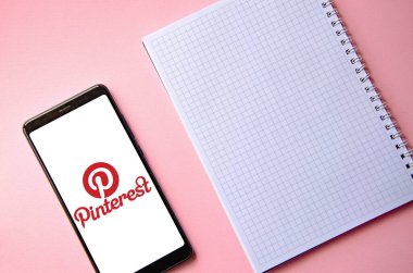 Pinterest. Ekrandaki akıllı telefon Pinterest mavi, pembe arka planda bir kalemle birlikte bir defterin üzerinde. Temmuz 2020. Kiev, Ukrayna.