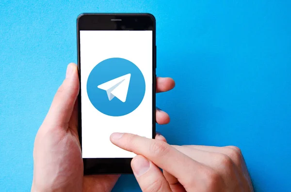 Telgraf var. Mavi, sarı, siyah arka planda bir telgraf akıllı telefonunun ekranında bir adamın elindeki akıllı telefon. Temmuz 2020. Kiev, Ukrayna.