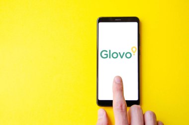 Glovo. Akıllı telefon ekranında Glovo yemek teslimatı. Sarı arka planda bir adamın elindeki akıllı telefon. Temmuz 2020. Kiev, Ukrayna.