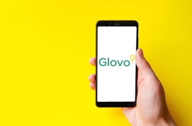 Glovo. Akıllı telefon ekranında Glovo yemek teslimatı. Sarı arka planda bir adamın elindeki akıllı telefon. Temmuz 2020. Kiev, Ukrayna.