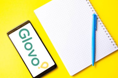 Glovo. Akıllı telefon ekranında Glovo yemek teslimatı. Sarı arka planda kalemi olan akıllı telefon ve defter. Temmuz 2020. Kiev, Ukrayna.