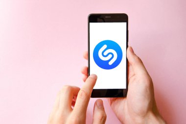 Shazam. Akıllı telefondan Shazam şarkısını tanımlamak için başvuru formu. Sarı, siyah, mavi, pembe arka planda bir adamın elindeki akıllı telefon. Temmuz 2020. Kiev, Ukrayna.
