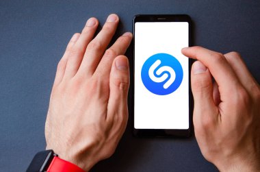 Shazam. Akıllı telefondan Shazam şarkısını tanımlamak için başvuru formu. Sarı, siyah, mavi, pembe arka planda bir adamın elindeki akıllı telefon. Temmuz 2020. Kiev, Ukrayna.