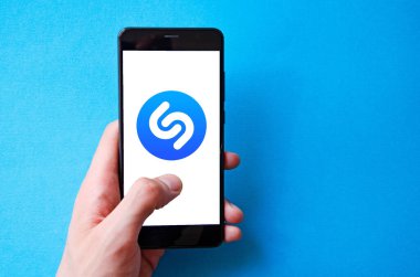 Shazam. Akıllı telefondan Shazam şarkısını tanımlamak için başvuru formu. Sarı, siyah, mavi, pembe arka planda bir adamın elindeki akıllı telefon. Temmuz 2020. Kiev, Ukrayna.