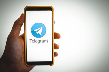 Telgraf var. Mavi, sarı, siyah arka planda bir telgraf akıllı telefonunun ekranında bir adamın elindeki akıllı telefon. Temmuz 2020. Kiev, Ukrayna.
