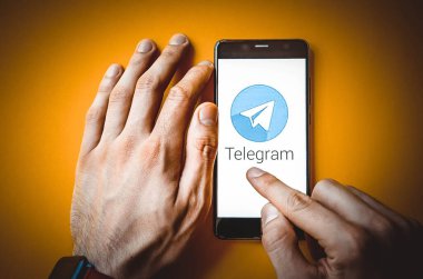 Telgraf var. Mavi, sarı, siyah arka planda bir telgraf akıllı telefonunun ekranında bir adamın elindeki akıllı telefon. Temmuz 2020. Kiev, Ukrayna.