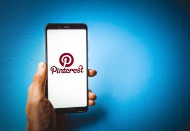 Pinterest. Mavi, sarı, siyah arka planda Pinterest akıllı telefon ekranında erkek eli ile akıllı telefon. Temmuz 2020. Kiev, Ukrayna.