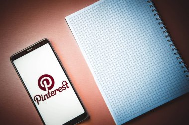 Pinterest. Ekrandaki akıllı telefon Pinterest mavi, pembe arka planda bir kalemle birlikte bir defterin üzerinde. Temmuz 2020. Kiev, Ukrayna.