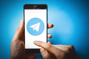 Telgraf var. Mavi, sarı, siyah arka planda bir telgraf akıllı telefonunun ekranında bir adamın elindeki akıllı telefon. Temmuz 2020. Kiev, Ukrayna.