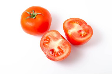 Beyaz arka plan ve üst manzarada iki kırmızı domates kuyruk yeşili olarak görülüyor. Bir domates bir bütün, diğeri de kesilmiş.