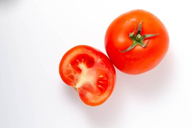 Beyaz arka plan ve üst manzarada iki kırmızı domates kuyruk yeşili olarak görülüyor. Bir domates bir bütün, diğeri de kesilmiş.