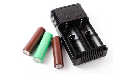 İki 18650 pil için siyah bir şarj aleti. Şarj olurken beyaz arka planda yeşil ve kahverengi bir batarya. Erkek eli pili şarj eder.