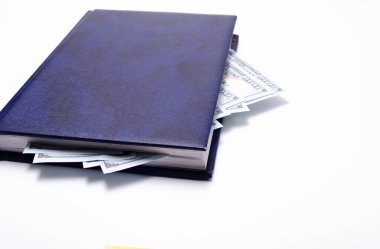 100 dolarlık banknotlar mavi bir defterde beyaz bir arka planda, yakın planda duruyor. Bir adamın eli dolarlarla bir defter açar. Zor günler için bir hisse senedi bul. Miras.