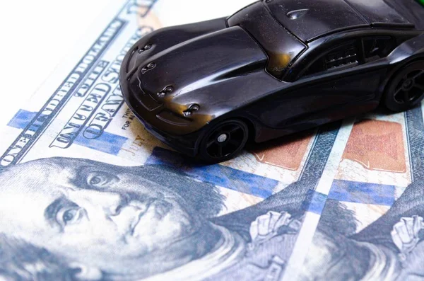 Siyah ve beyaz arka planda bir yığın banknotun üzerinde siyah oyuncak araba. Yeşil spoiler 'ı olan bir spor araba, yakın çekim ve yan görüntüde dolar üzerine bir kanat. Arka ve ön vagon. Satıyorum, alıyorum.