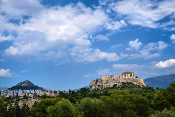 Ikonischer Blick auf den Akropolis-Hügel und den Lycabettus-Hügel im Hintergrund in Athen, Griechenland vom Pnyx-Hügel im Sommertaglicht mit großen Wolken am blauen Himmel. — Stockfoto