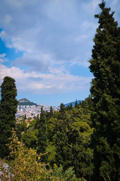 Vista de la colina de Lycabettus desde la colina de Areopagus con el follaje rico y los árboles altos del cedro o del ciprés. Atenas, Grecia. Día de verano y cielo azul con nubes — Foto de Stock