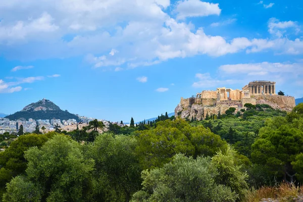 Ikonischer Blick auf den Akropolis-Hügel und den Lycabettus-Hügel im Hintergrund in Athen, Griechenland vom Pnyx-Hügel im Sommertaglicht mit großen Wolken am blauen Himmel. — Stockfoto