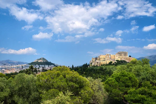 Ikonischer Blick auf den Akropolis-Hügel und den Lycabettus-Hügel im Hintergrund in Athen, Griechenland vom Pnyx-Hügel im Sommertaglicht mit großen Wolken am blauen Himmel. — Stockfoto