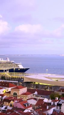 Büyük yolcu gemisi limandan ayrılıyor ve rıhtımdan geçiyor. Gün batımında alacakaranlık, bulutlu, dramatik gökyüzünün mor renkleriyle. Alfama, şehrin en eski kısmı, ön planda ve arka planda Tagus nehri. Yaz tatili, tatil havası, gezi.