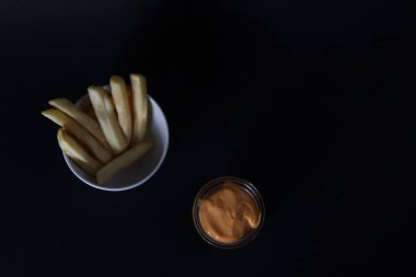 Bir kase patates kızartması ve siyah arka planda izole edilmiş bir kase peynir sosu. Resim kopyalama alanı içeriyor
