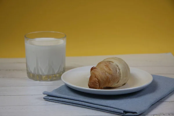 羊角面包放在盘子里的蓝色餐巾上 牛奶放在木制桌子上 图像包含复制空间 — 图库照片