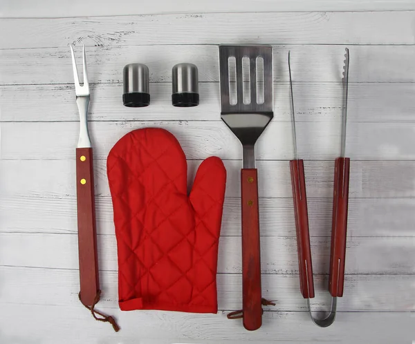 BBQ instruments kit (tongs, glove, knife, fork, spatula, peper and salt shakers) close up isolated on white wooden background flat lay