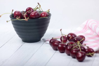 Siyah böğürtlen kasesi, bir yığın kiraz ve beyaz ahşap arka planda bir havlu. Resim kopyalama alanı içeriyor