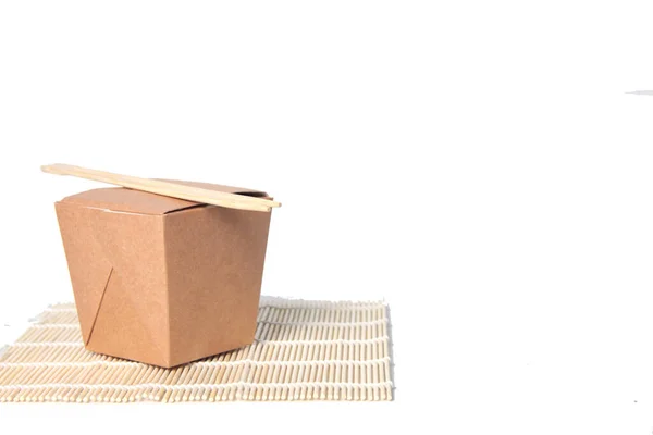 Wok box ve Çin ahşap çubukları beyaz arka planda izole edilmiş bir hasırın üzerinde. Resim kopyalama alanı içeriyor