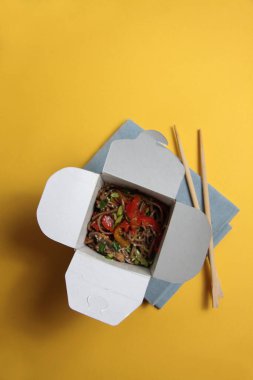 wok box ve yemek çubukları sarı arka planda izole edilmiş. Resim kopyalama alanı içeriyor