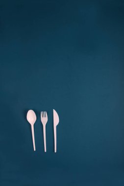 Mavi arka planda plastik kaşık, çatal ve bıçak. Dikey görüntü. Resim kopyalama alanı içeriyor