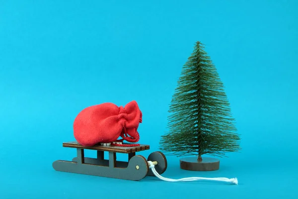 青い背景に孤立したモミの木によってそりで完全なサンタクロースの赤い袋 クリスマスのギフトの概念 画像にはコピースペースがあります — ストック写真