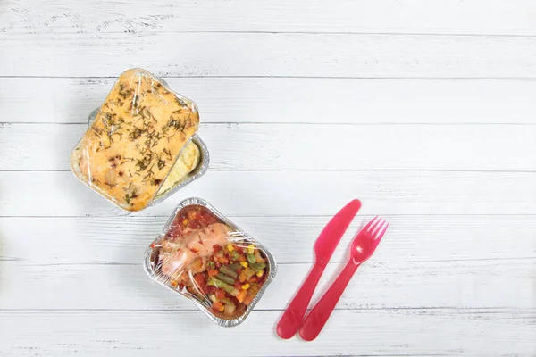 delivery menu concept - pile of foil boxes, knife and fork on white wooden background flat lay. Take away of organic daily meal, copy space