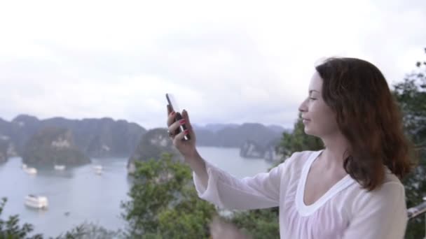 旅行でオンラインであります 近代的な技術と通信します 背景が海と島の丘の上に Selfie を行う若い女性 — ストック動画