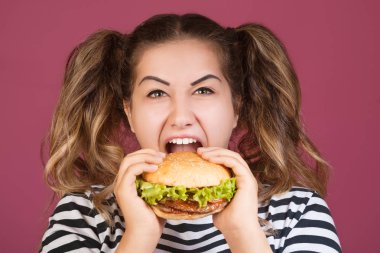 Genç kız mutlu yüz ve Aç açık ağzı ile sığır eti burger sandviç tutarak pembe arka plan izole. Fast food kavramı.