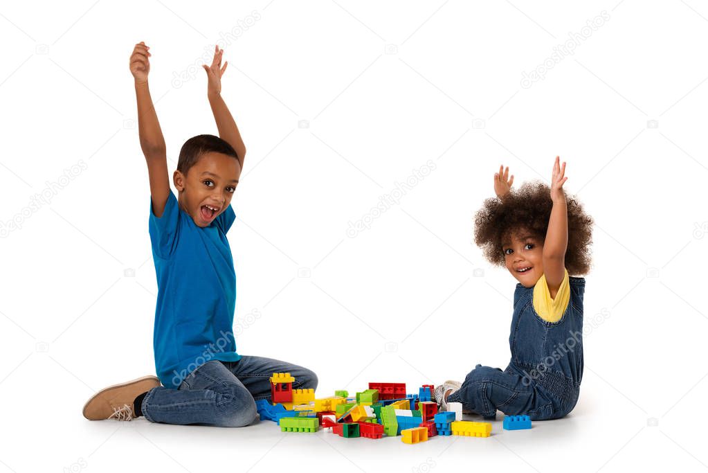 Two little cute african american children playing on the floor with lots of colorful plastic blocks in studio, isolated on white background