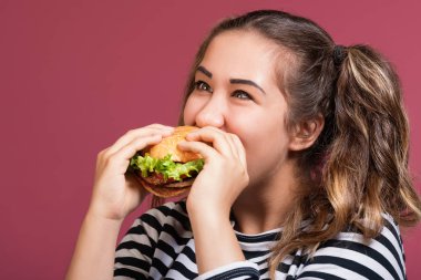 Çizgili tişört yeme hamburger iştahla pembe renkli arka plan üzerinde deli komik serin kız