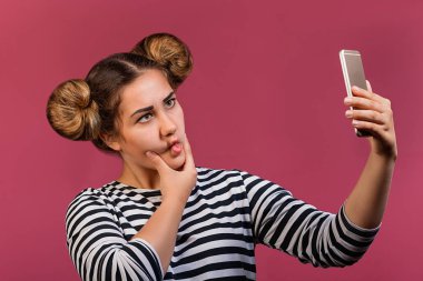 Öğrenci hippi kız selfie fotoğraf üstünde hareket eden telefon, pembe arka plan üzerinde yapım komik saç ve yüz ifadesi ile izole. Olumlu ruh hali