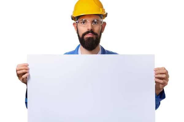 Hombre barbudo guapo trabajador en casco protector sosteniendo pancarta publicitaria blanca con espacio de copia, aislado sobre fondo blanco . — Foto de Stock