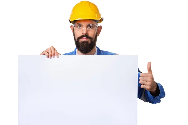 Builder worker in protective construction helmet raising his thumbs up and holding white advertising board with copy space, isolated — Stock Photo, Image